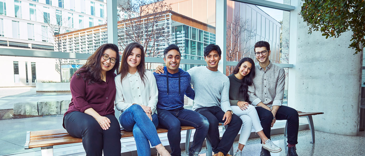 A group of student sit on a bench smiling