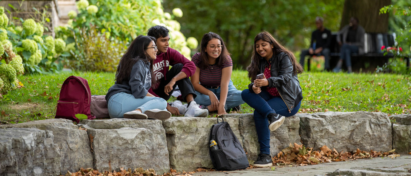 A group of McMaster student sit on the grass and rocks outside