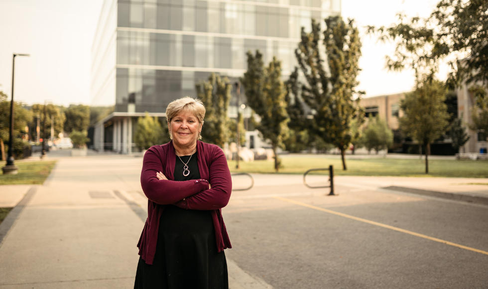 A smiling Heather Sheardown with her arms crossed, standing on campus with a building in the background.