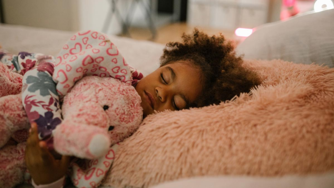 A young girls holds a stuffed elephant as she sleeps in her bed.