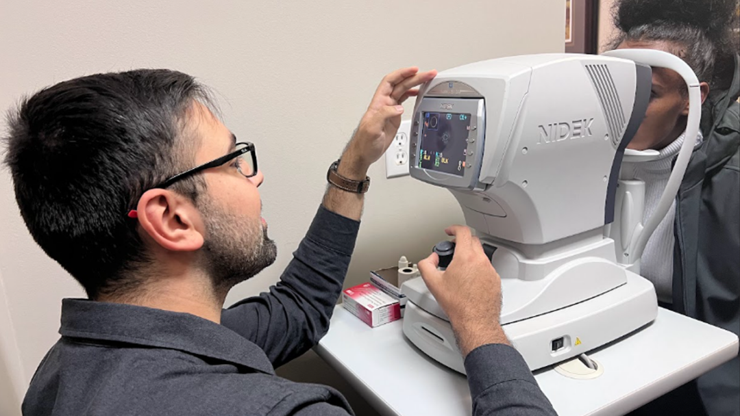 A medical learner, Amin Hatamnejad, performs an eye exam on a patient at the refugee vision screening clinic.