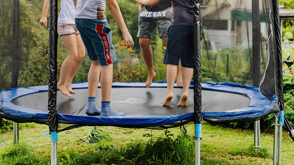 A group of four friends jump on a trampoline that has been place on grass.