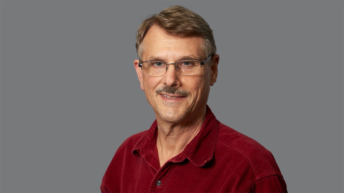 Gordon Guyatt can be seen in this image wearing glasses and a red collard shirt.
