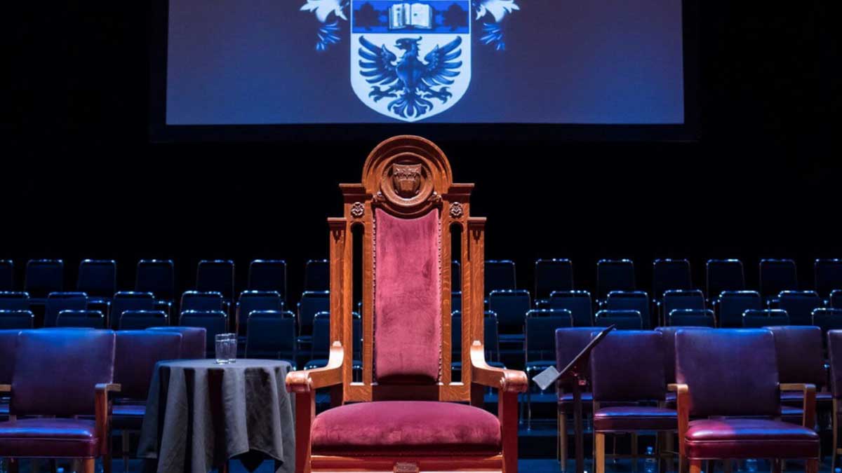 Image of red chair with wooden arm rests on a stage.
