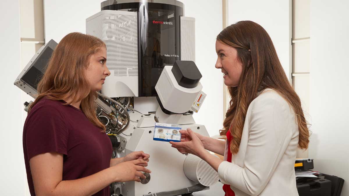 Two engineering researchers talking in front of an electron microscope
