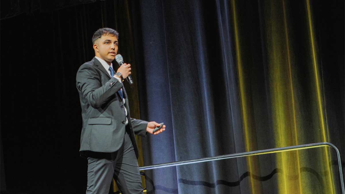 Mann Parikh wearing a suit, holding a mic at a competition.