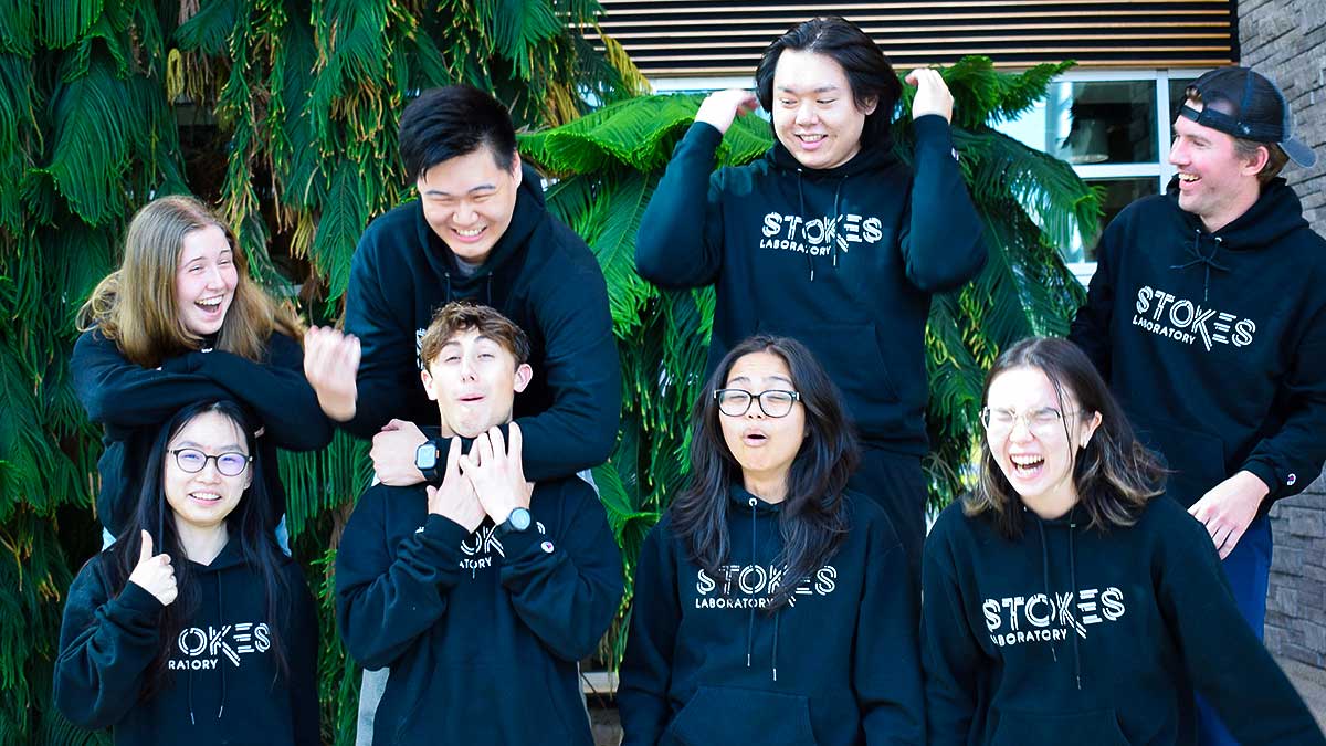 A group of young people wearing black sweatshirts, standing together and posing for a photo.