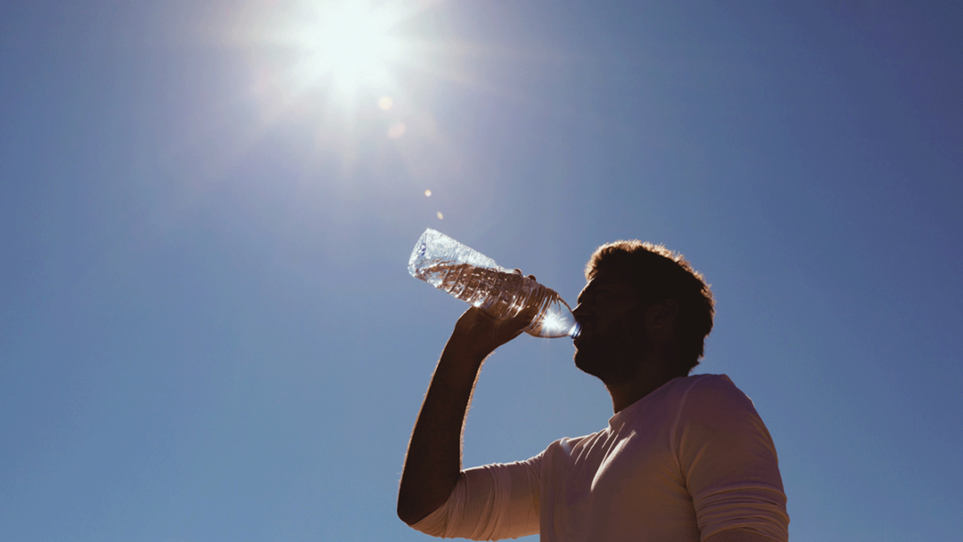 A man drinks from a water bottle below a blue and sunny sky.