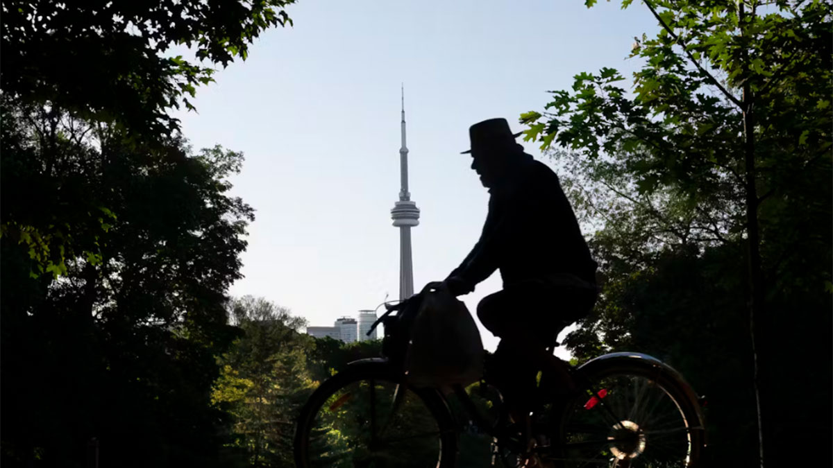 The silhouette of a man on a bicycle set against a backdrop of greenery. Toronto's CN Tower can be seen in the background.