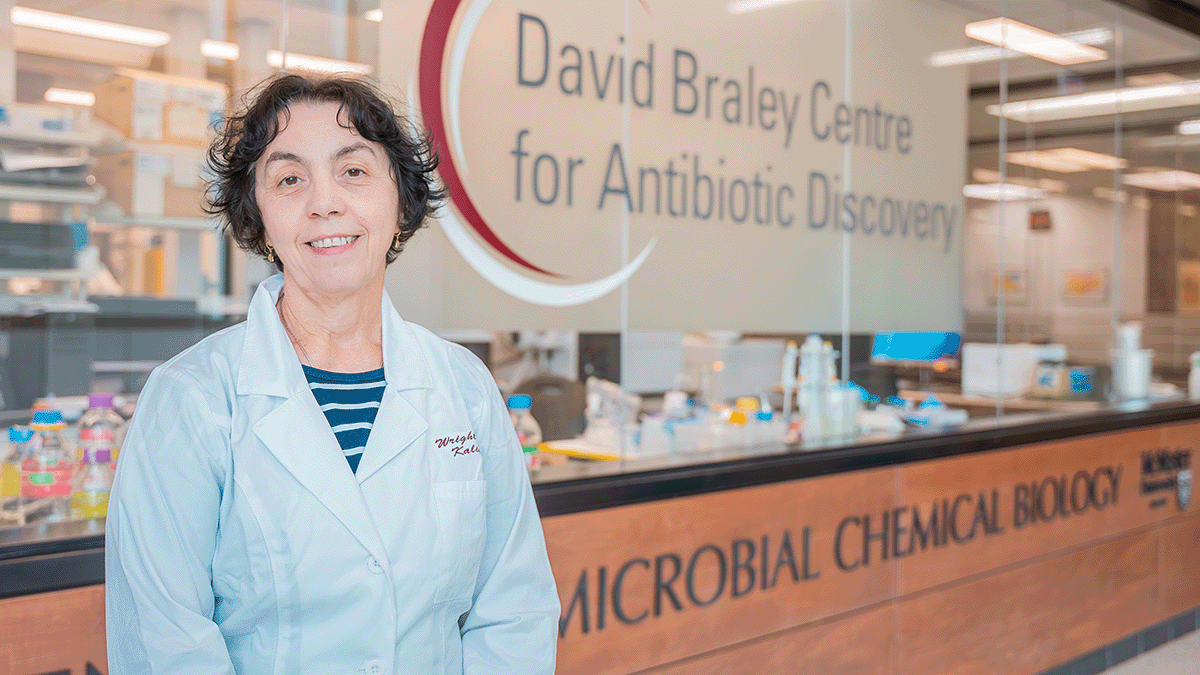 Kalinka Koteva can be seen wearing a lab coat while standing in front of a sign for the David Braley Centre for Antibiotic Resistance.