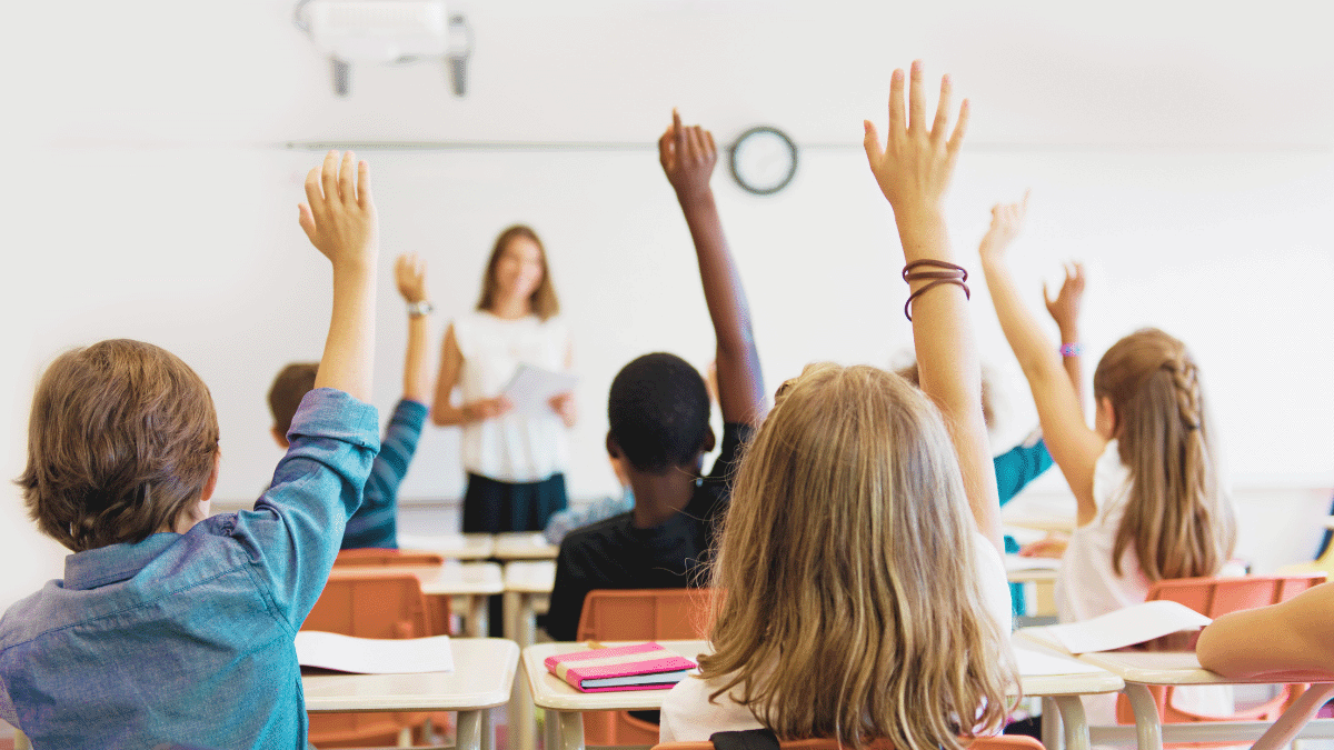 Several students raise their hands while seated in a classroom.