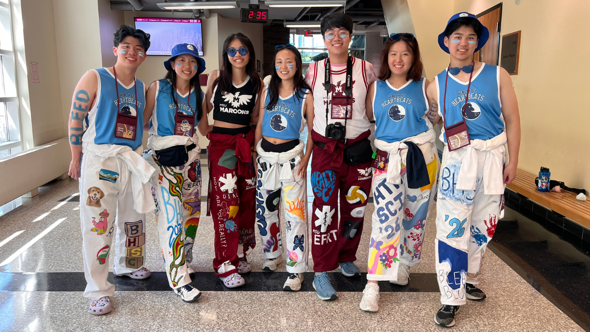 A group of Welcome Week reps standing together, smiling and wearing their program jumpsuits, in the Michael G. DeGroote Centre for Learning and Discovery.