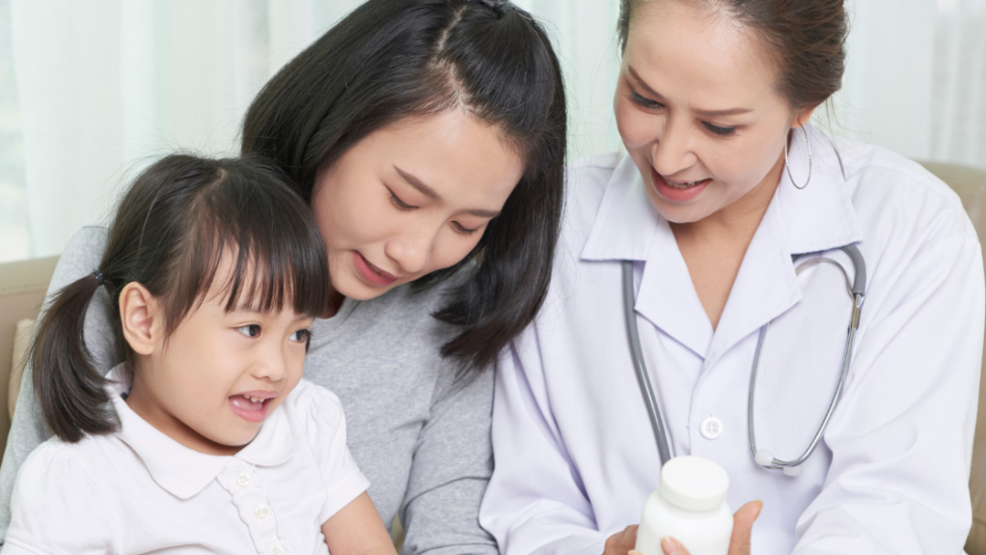 A doctor holds a pill bottle while sitting next to a women and a young girl.