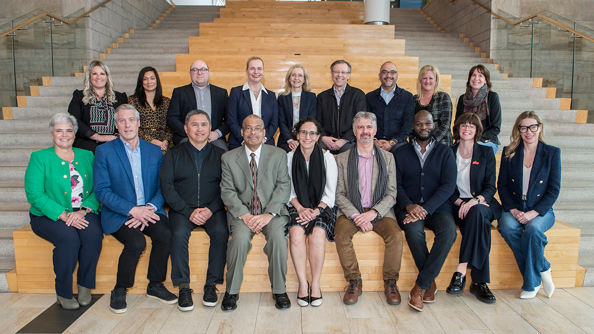 A group photo of 18 senior leaders who participated in the first cohort of the National Health Fellows program. The first row is sitting on steps, the second row is standing behind them.