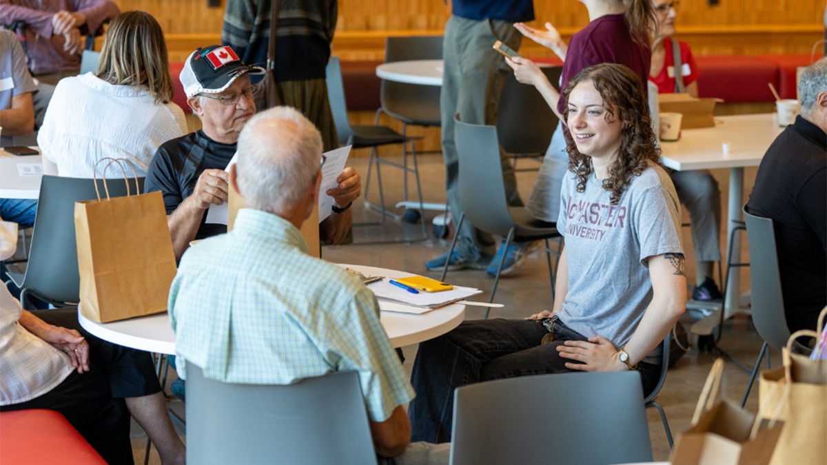 A student in a McMaster t-shirt seated at a table engaged in conversation with two older adults