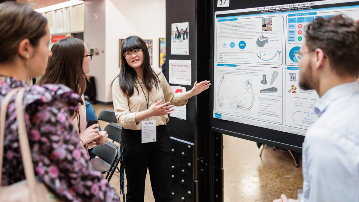 A person explains their poster presentation to 3 people at a previous Innovation Showcase.