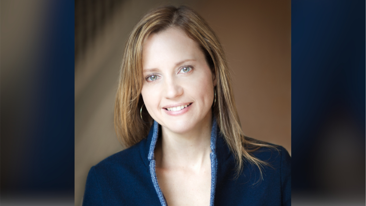 Samantha Nutt, smiling with brown hair, in a blue blazer over a white top, against a dark background.