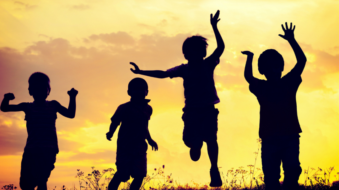 A group of children can be seen silhouetted by the sun, playing outside.