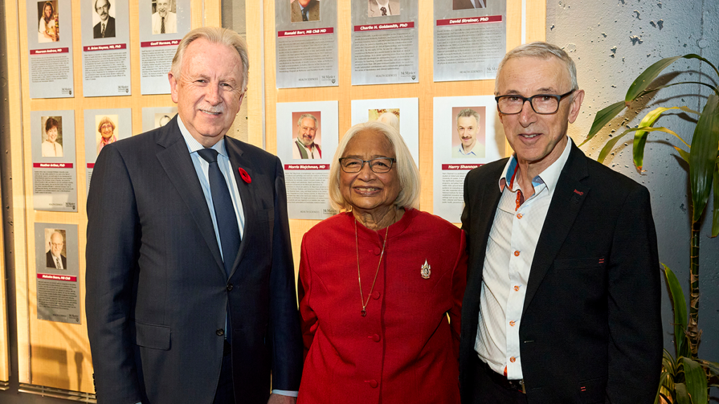 Three people stand by a display wall; the center person wears red, the others are in suits.