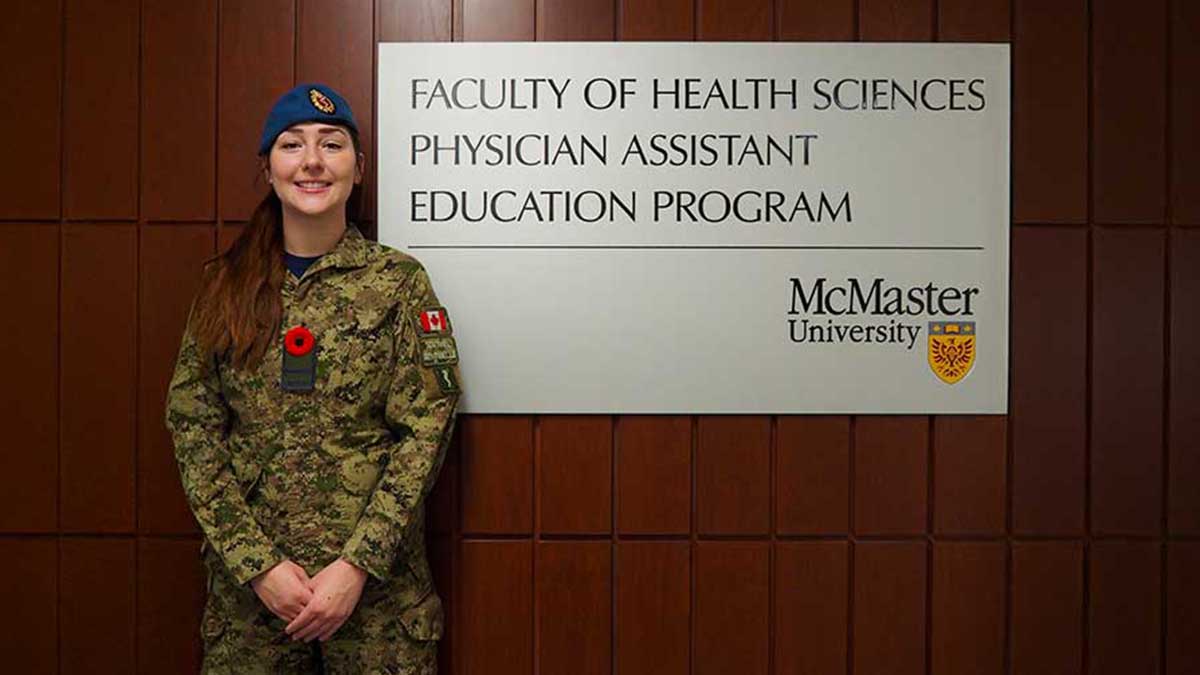 Officer Cadet Marissa Nociar stands in uniform with a poppy, by the PA Education Program sign.