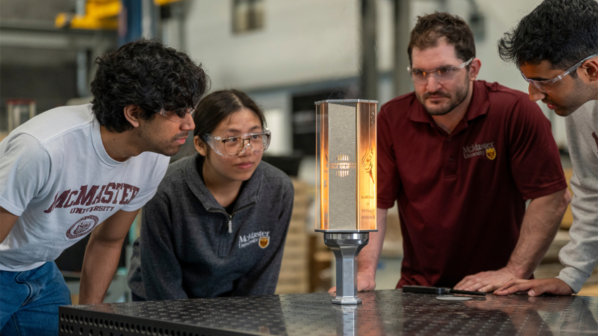 Four people in protective glasses intently observing a commemorative torch.