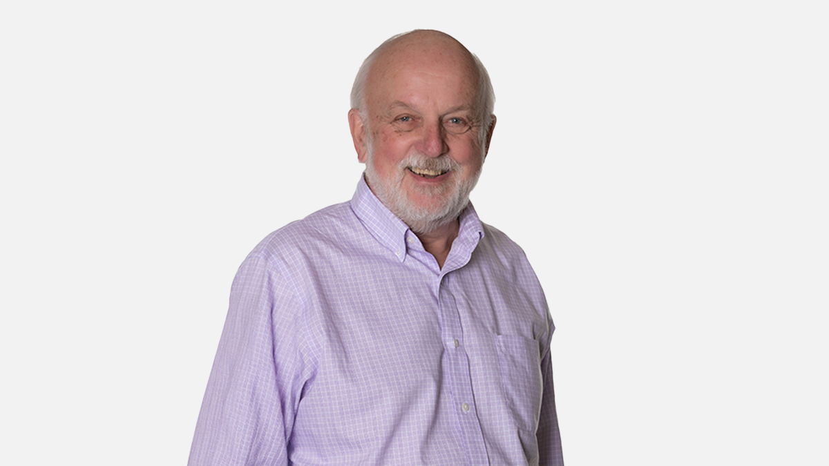 A headshot of Geoffrey Norman. He is wearing a purple dress shirt and is smiling for the photo.