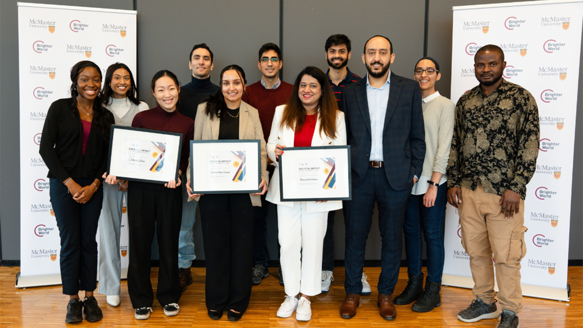 Smiling students pose indoors with McMaster banners; three hold award certificates.