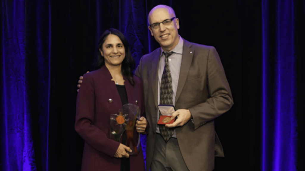 Sonia Anand stands on a stage with Michael Hill