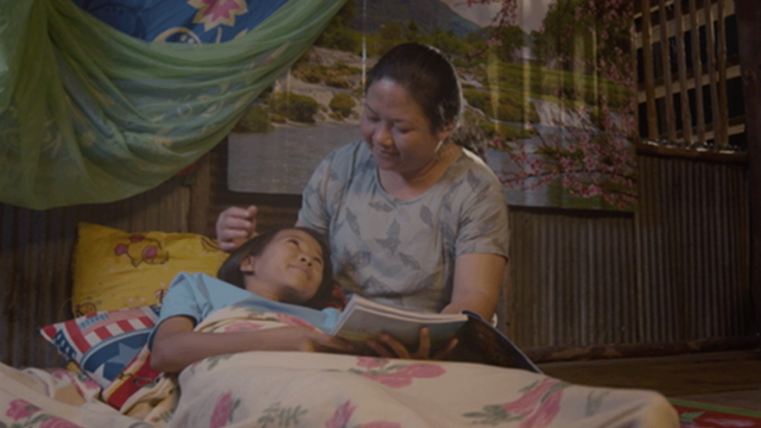 A woman can be seen reading to her child in a still from the “Being Family” film.